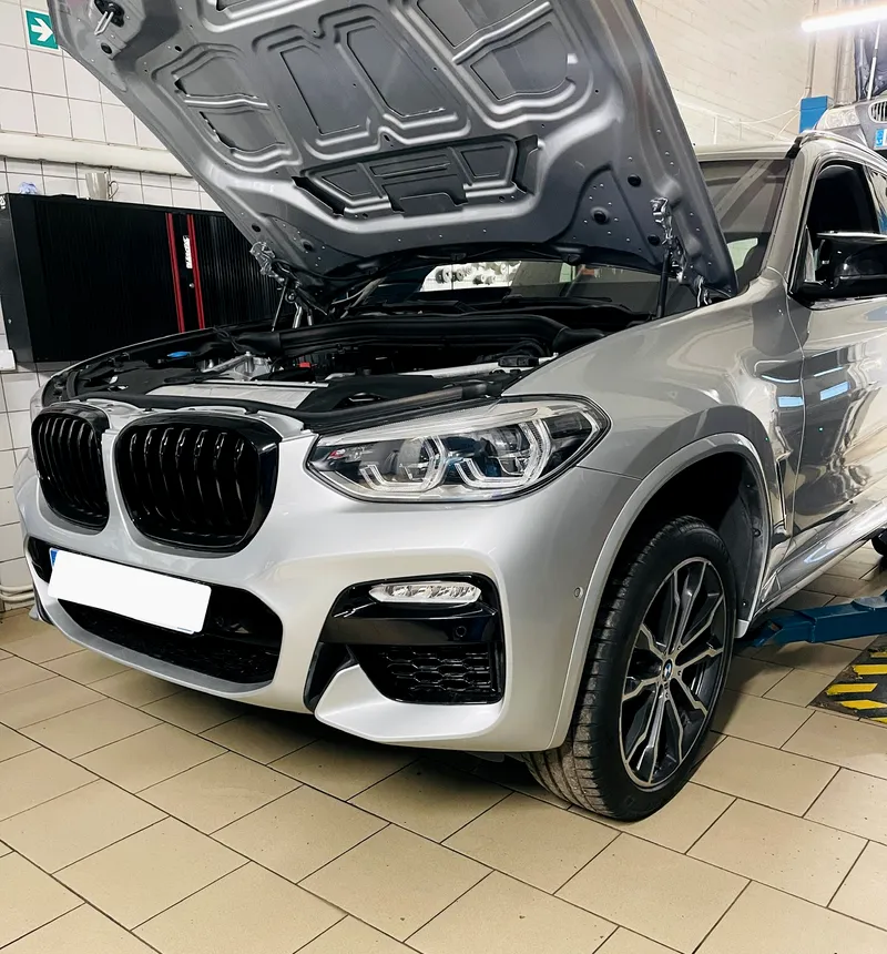 Sidabrinis BMW X3 su atidarytu variklio dangčiu ant keltuvo Autvadita servise Vilniuje