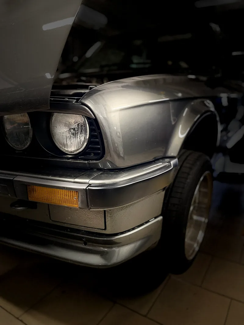 Klasikinis BMW su apvaliais žibintais ir atidarytu variklio dangčiu serviso patalpoje