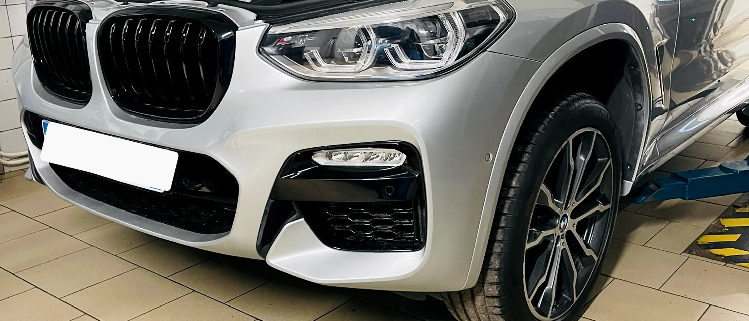 Sidabrinis BMW X3 su atidarytu kapotu ant keltuvo Autvadita servise