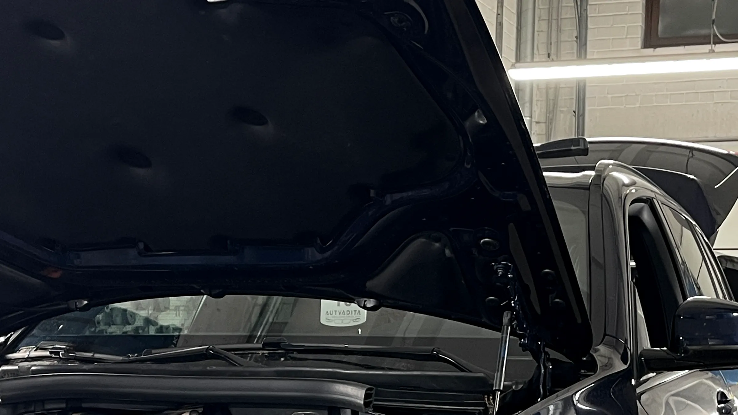Tamsiai mėlynas BMW X5 hibridas ant keltuvo su atidarytu kapotu ir oranžiniais aukštos įtampos kabeliais