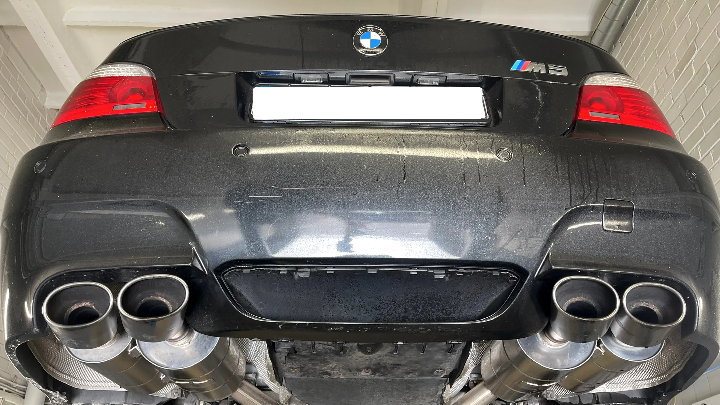 Juodo BMW M5 galas ant keltuvo servise, matomi keturi išmetimo vamzdžiai